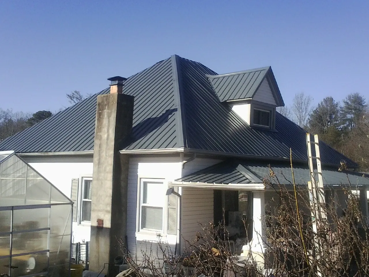 Dark blue standing seam metal roof on a white farmhouse with dormer — Slate & Tile Roof Repair by Roofing Brothers in Gonzales