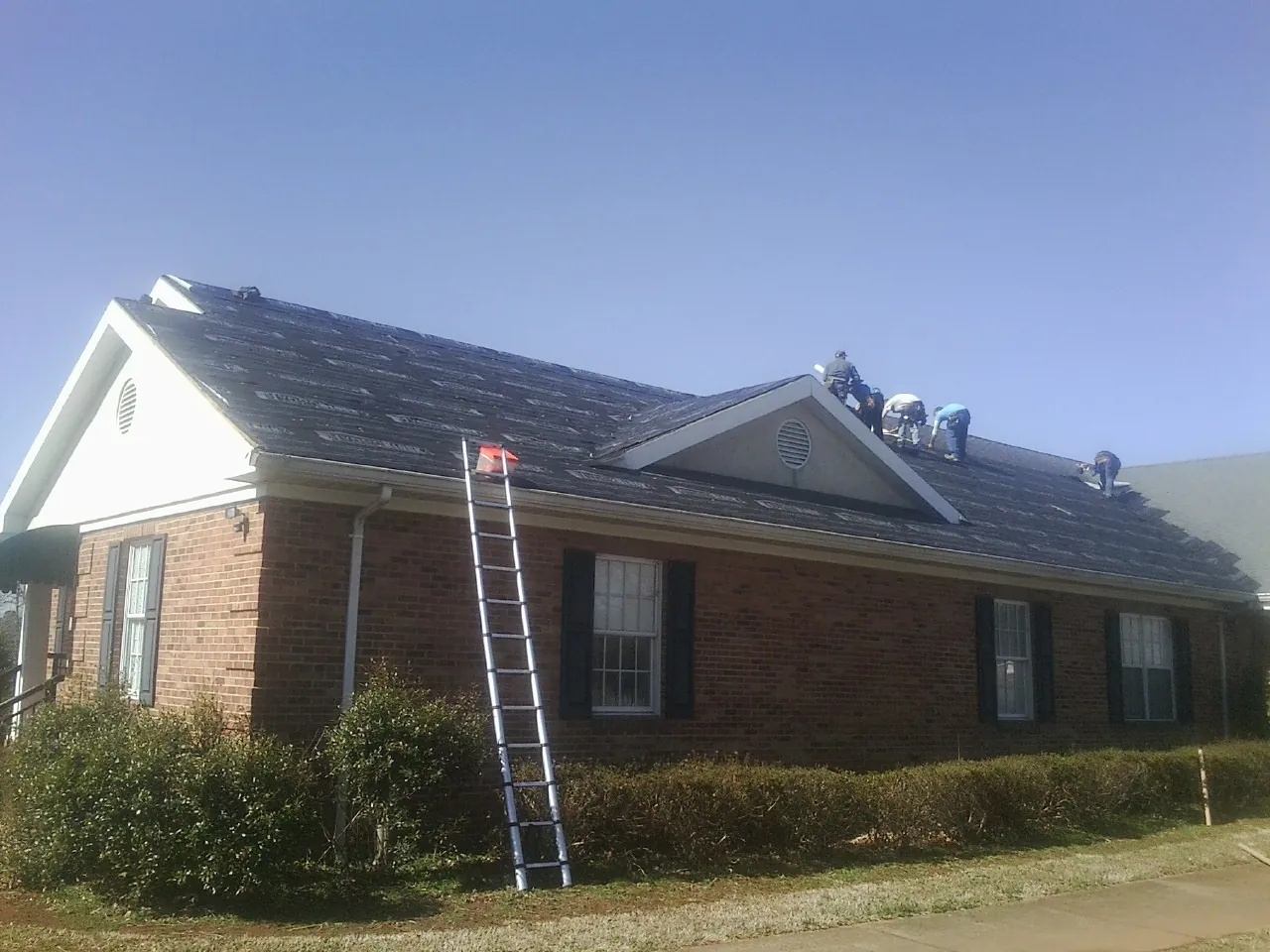 Crew tearing shingles off a brick ranch roof with a ladder set — Metal Roof Repair work by our crew in Gonzales