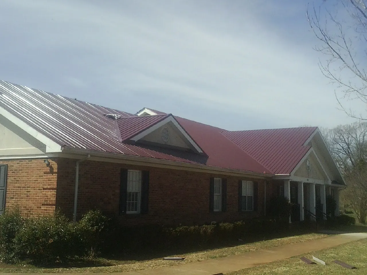 Red metal roof with gabled entries on a long brick building, from a Hail Damage Roof Repair job in Gonzales