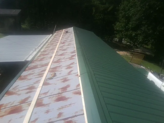 Old rusted panels beside newly installed green metal roofing — Wind Damage Roof Repair by Roofing Brothers in Gonzales