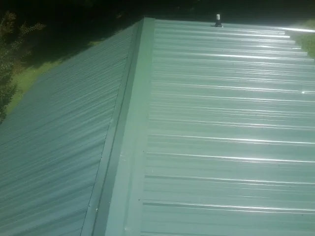 New green metal panels meeting at the ridge of a roof — Flat Roof Repair work by our crew in Gonzales