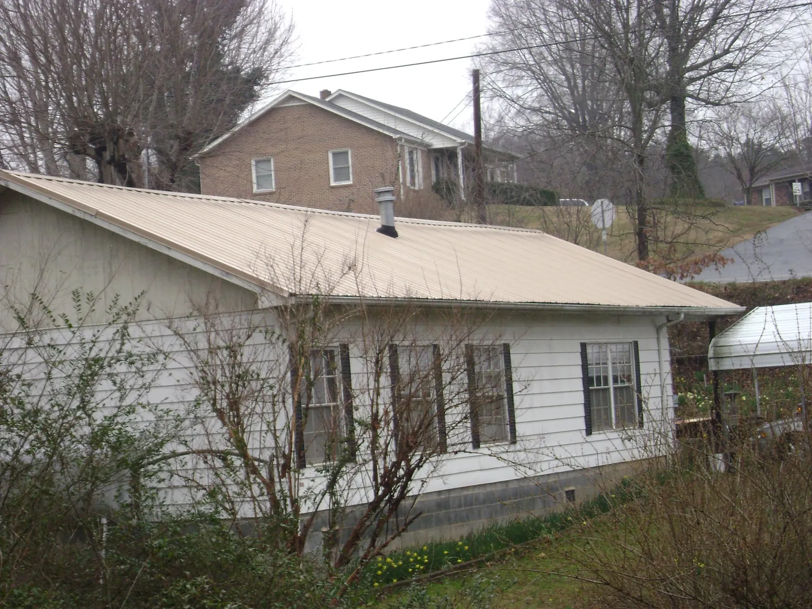 Tan metal roof on a white sided house set into a hillside — Commercial Roofing by Roofing Brothers in Gonzales